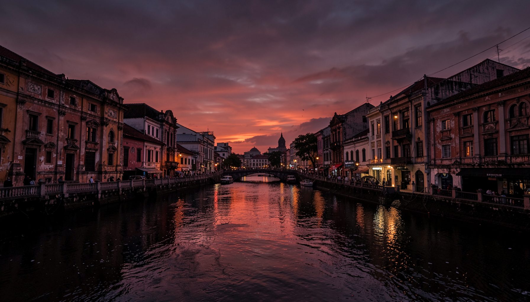 Dramatic wide view of the Jembatan Merah area in Surabaya at dusk, with deep red and amber tones reflecting off old colonial buildings